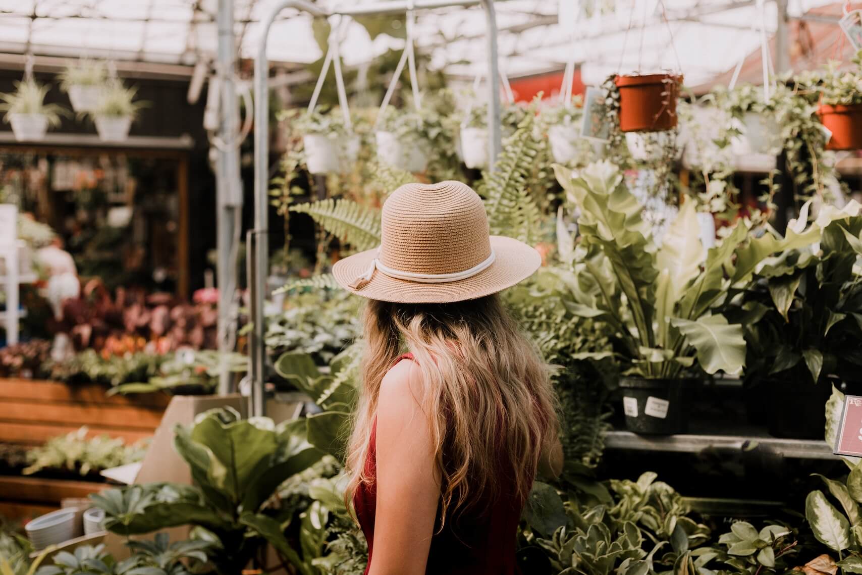 A person wearing a straw hat standing in a greenhouse garden shop.