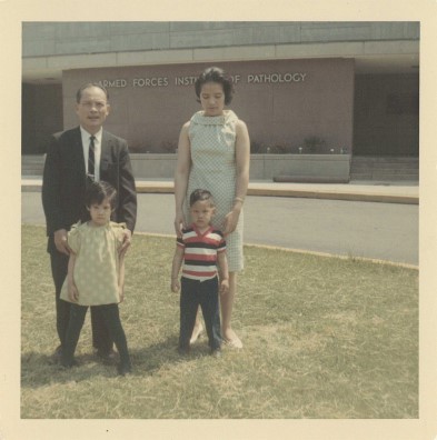 An antique photo of 2 parents and their children in front of a building.
