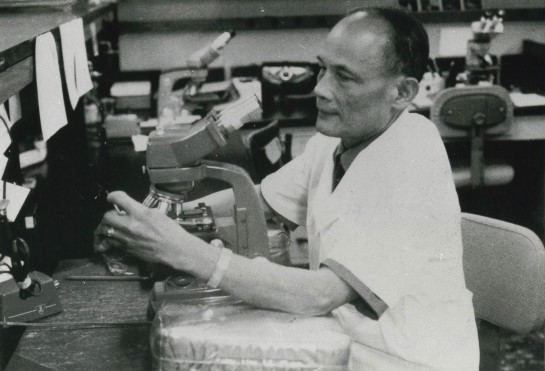 An antique black and white photo of a man working with a microscope.