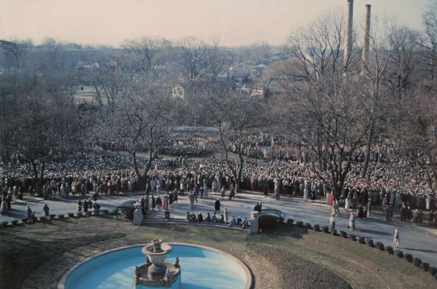 An antique image of a large crowd in front of a fountain in a park.