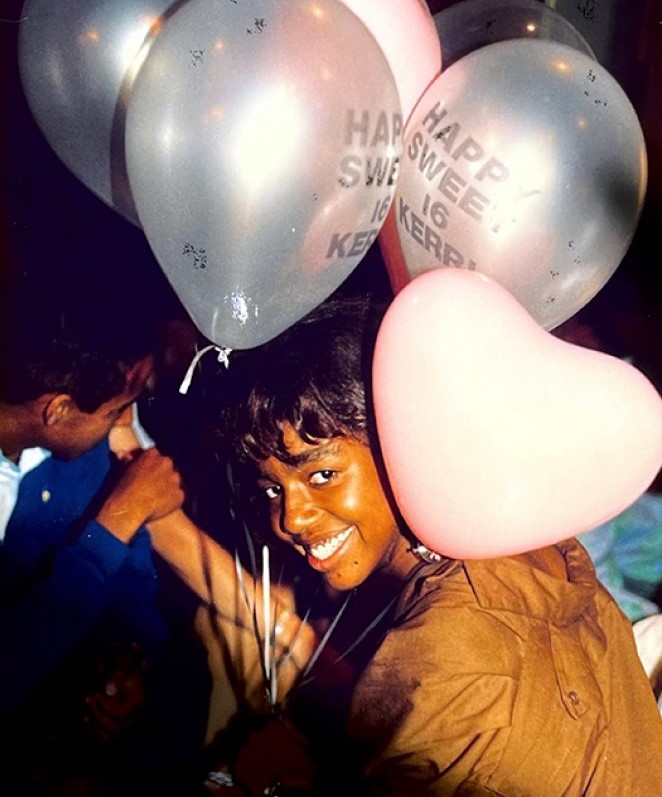A woman smiles at the camera holding balloons.